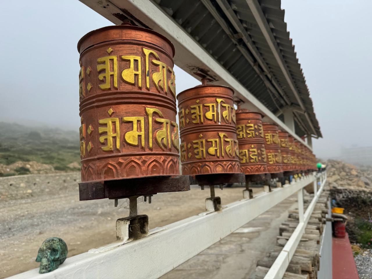 Row of copper prayer wheels beside the inn