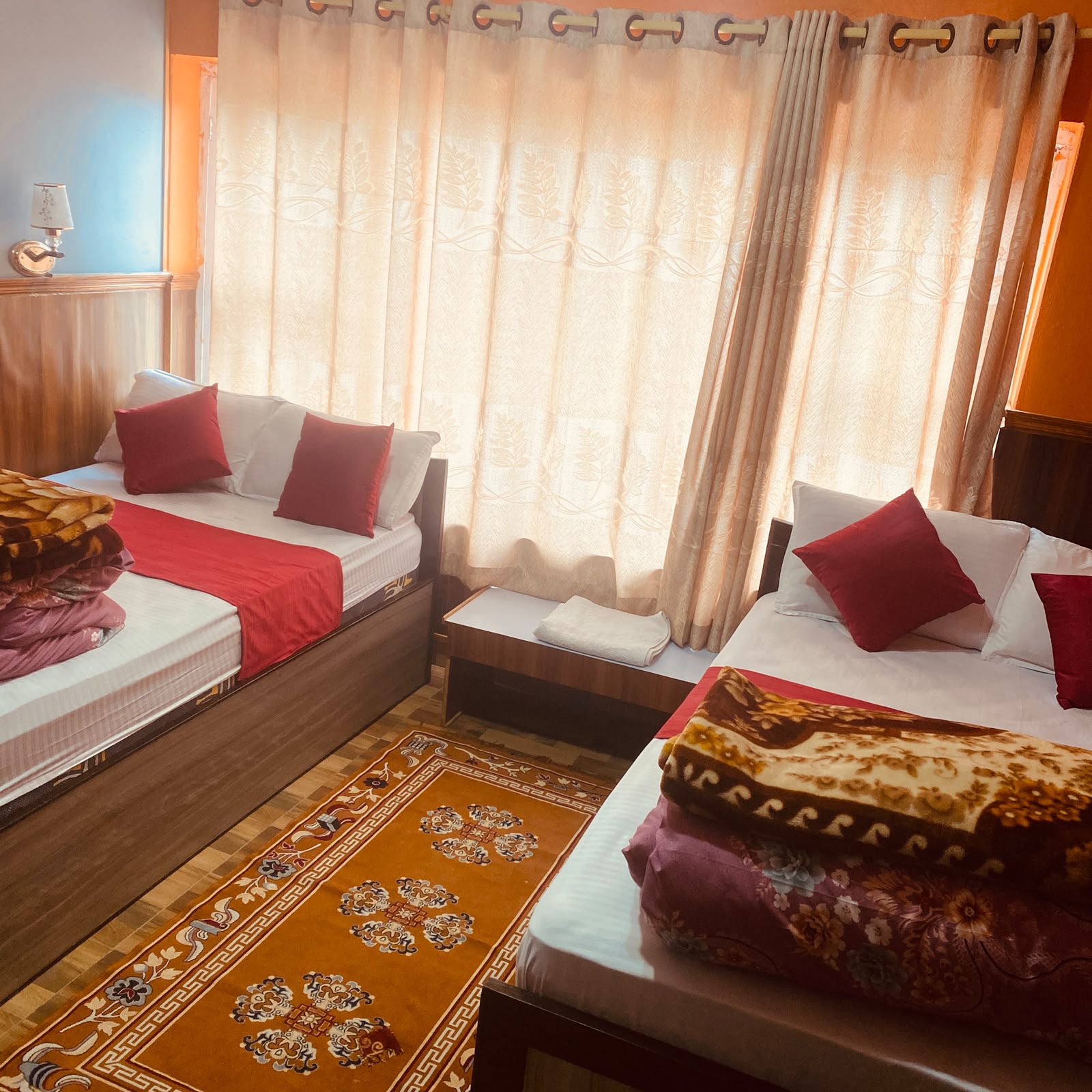Standard twin room: two single beds with red cushions, a big curtained window and a Tibetan rug